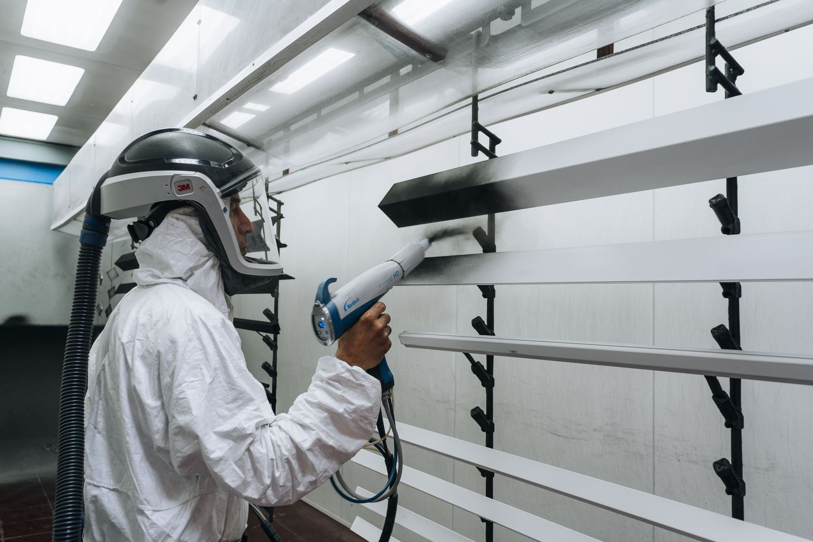 Medewerker in beschermpak spuit poedercoating op profielen